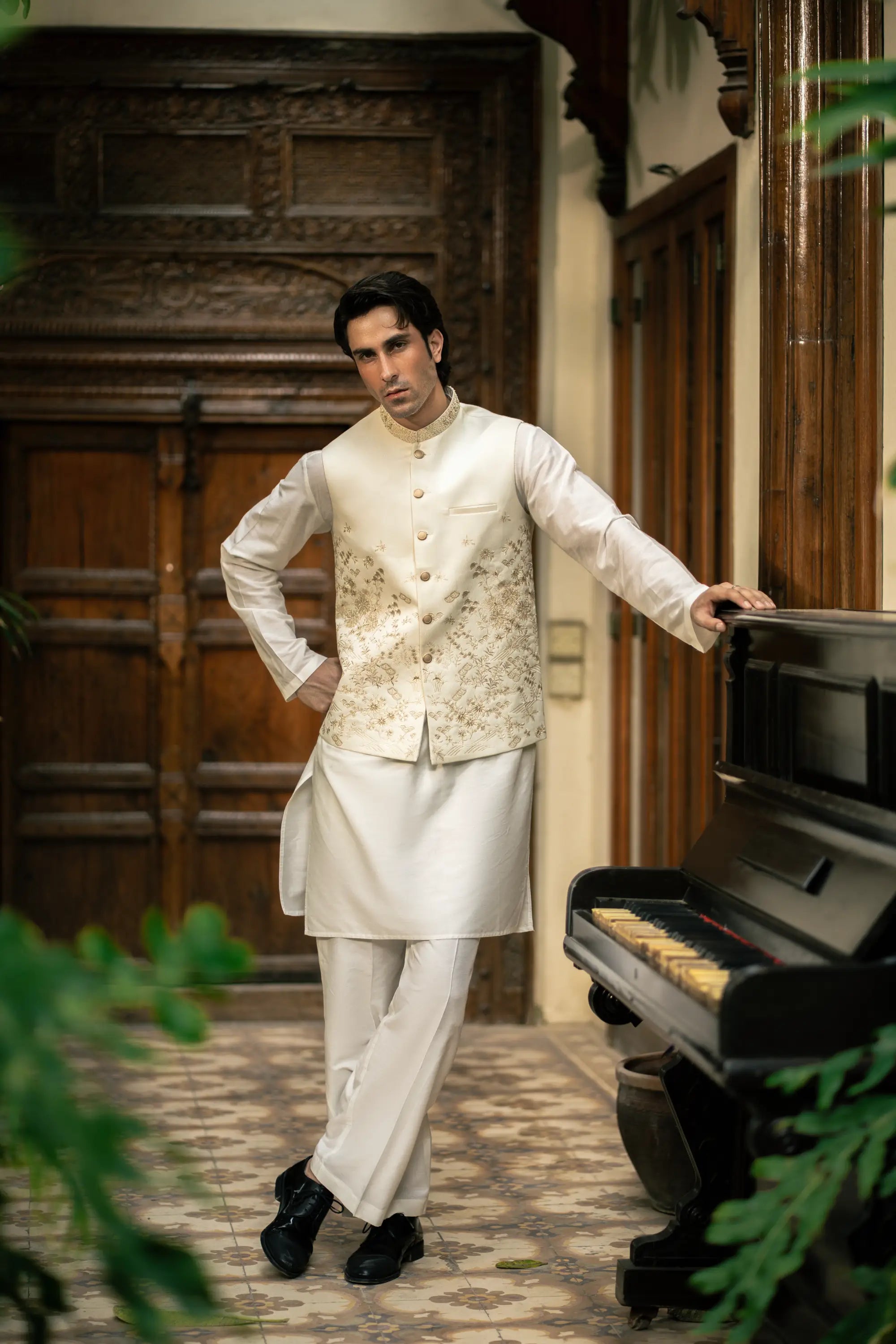 Man in traditional white outfit standing next to a piano in an elegant interior setting