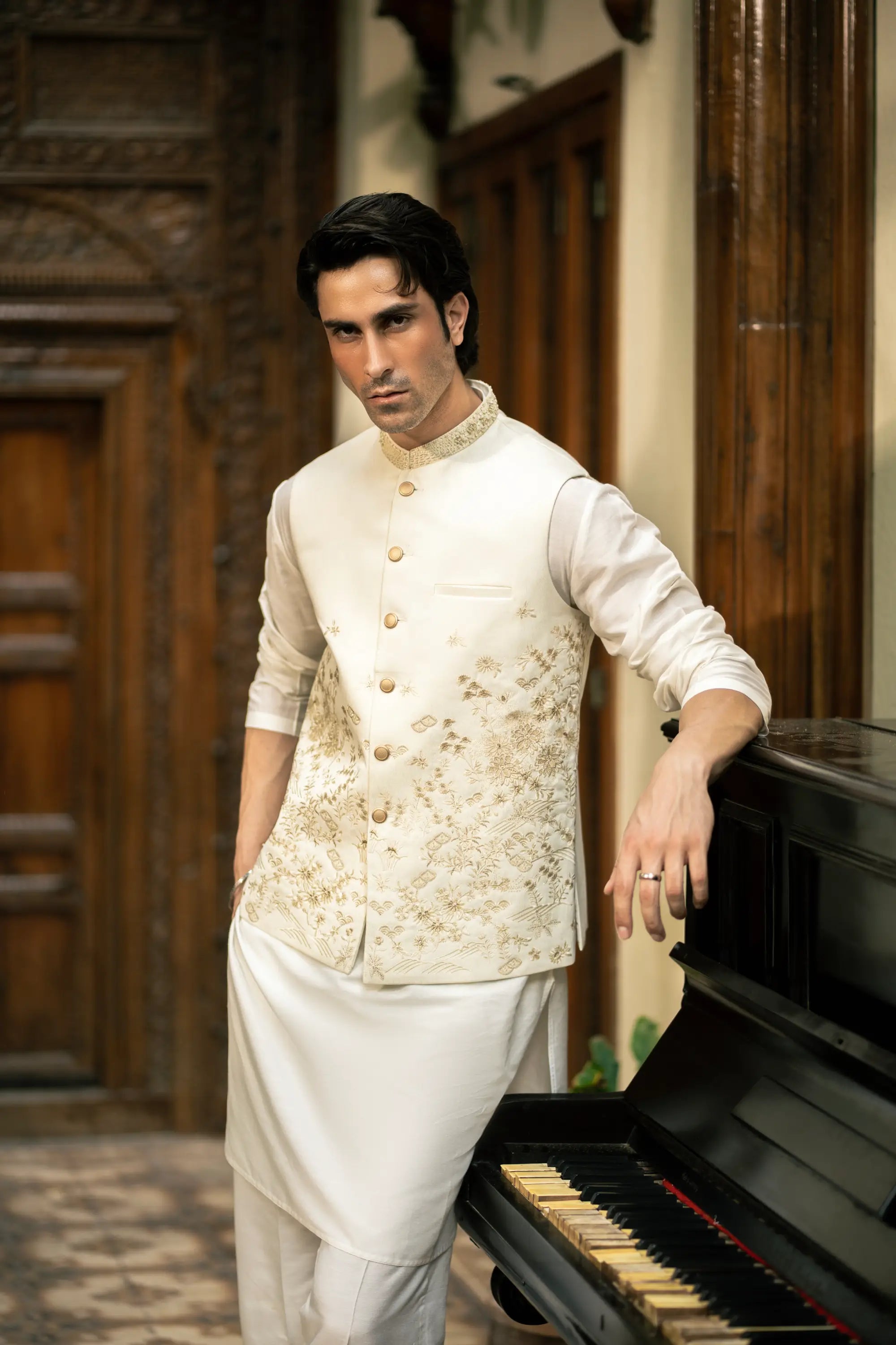 Man in traditional attire standing next to a piano in an ornate room.