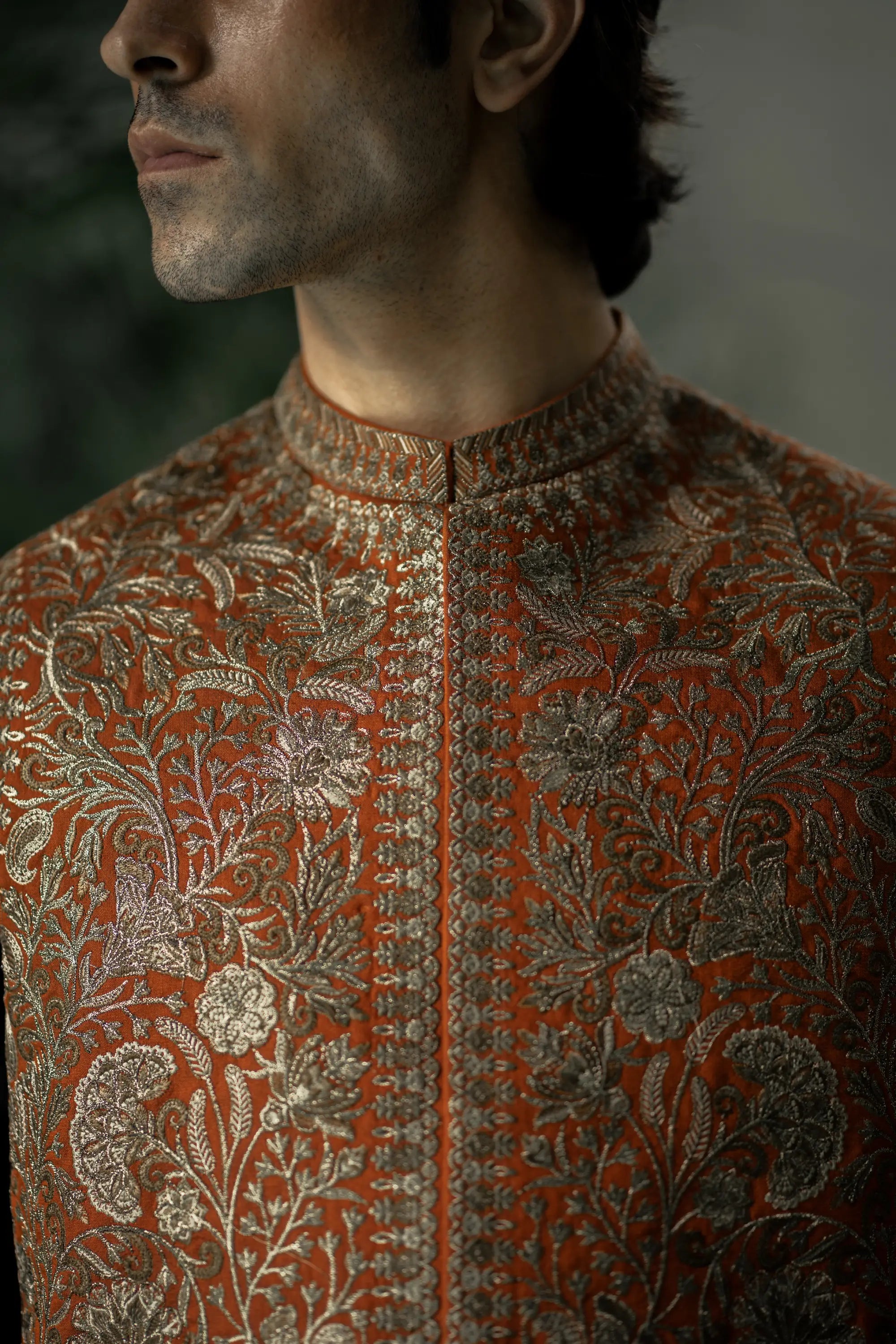 Close-up of a man wearing an intricately patterned orange and brown traditional outfit.