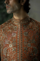 Close-up of a man wearing an intricately patterned orange and brown traditional outfit.