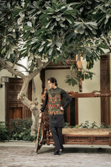 Man standing under a large tree in an outdoor setting with wooden furniture and plants.