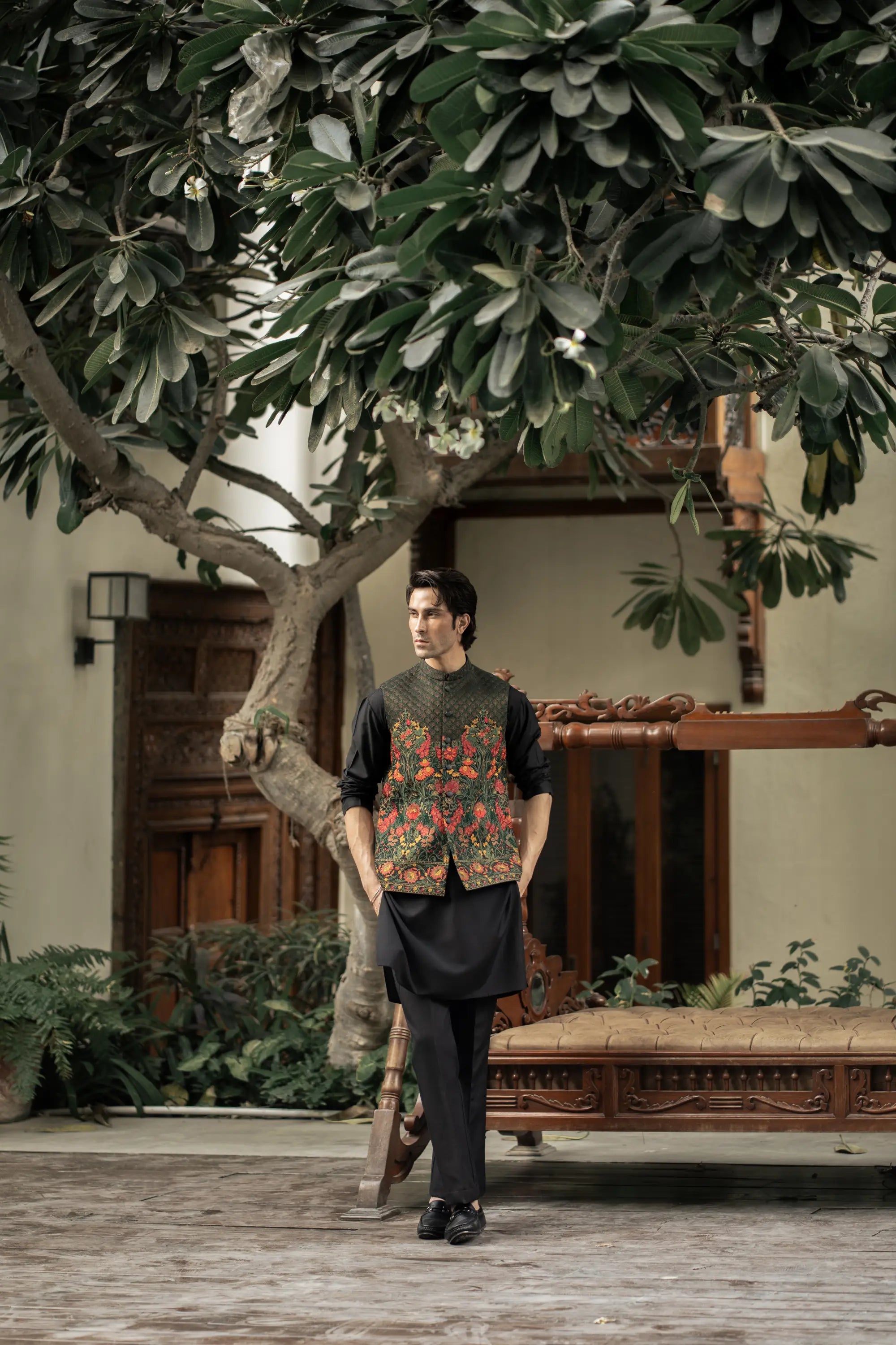 Man standing in a garden with a tree and traditional wooden bench in the background
