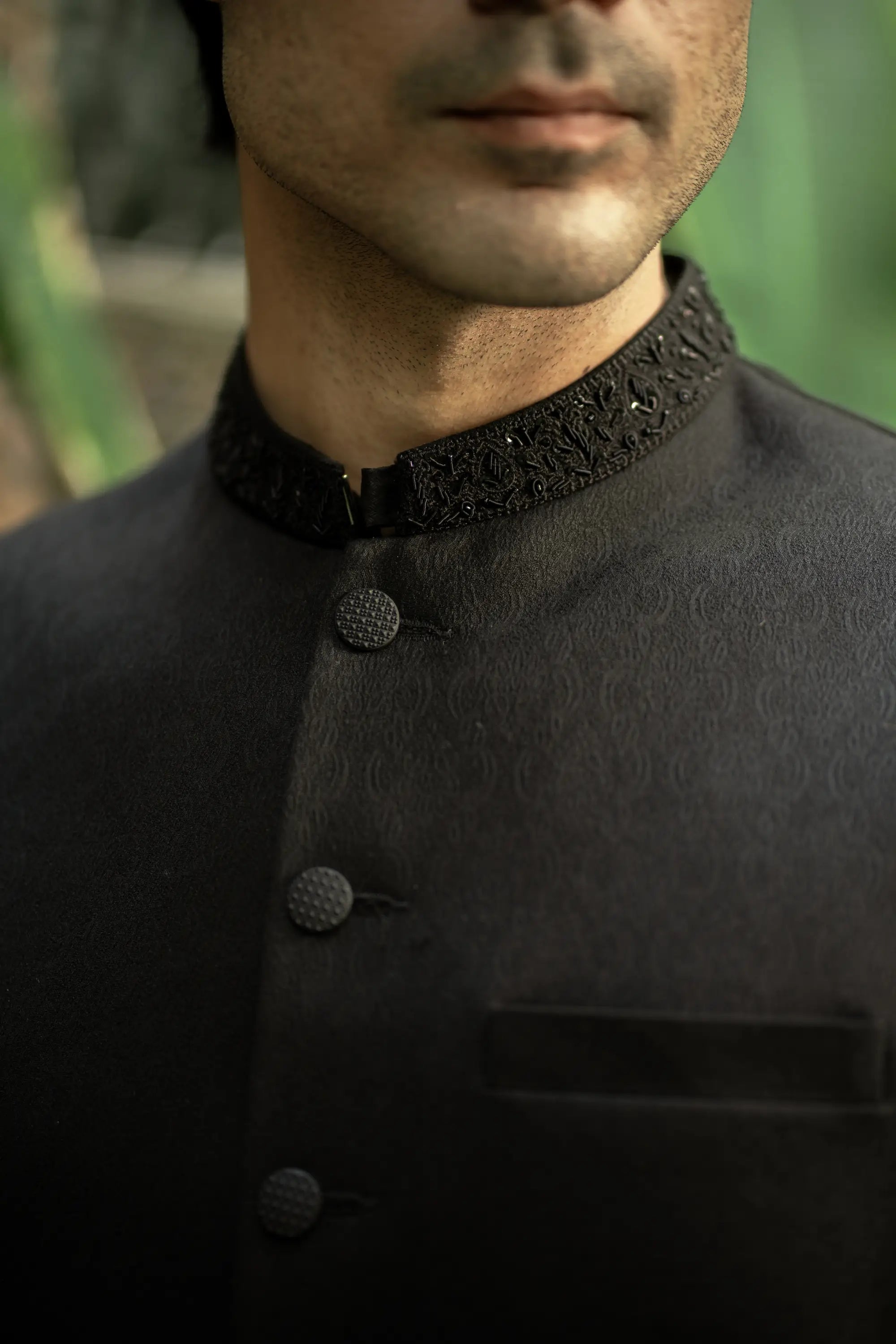 Man wearing a black traditional outfit with intricate collar design.