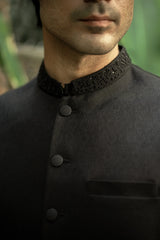 Man wearing a black traditional outfit with intricate collar design.