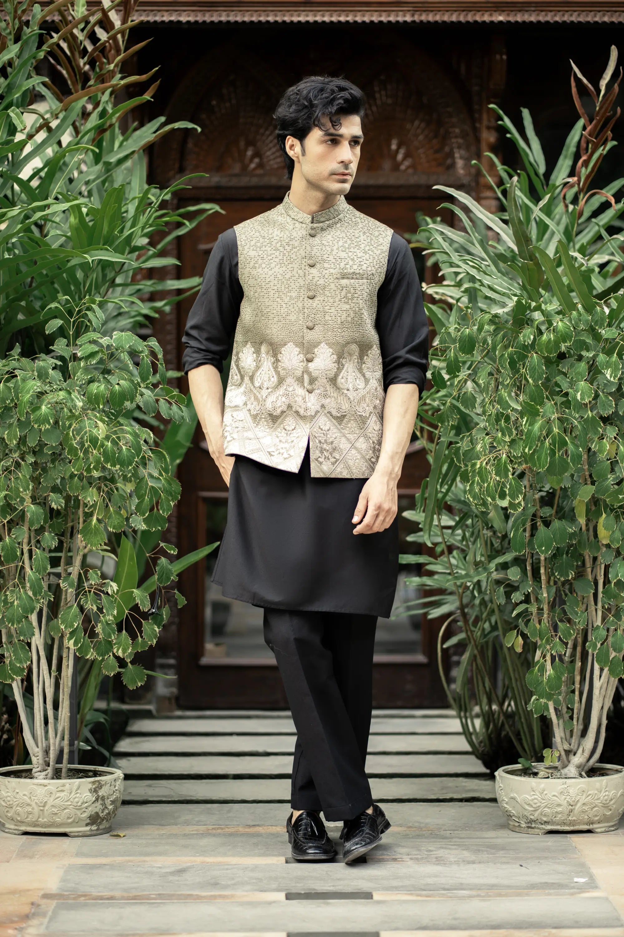 Man wearing a traditional outfit with a vest in a garden setting