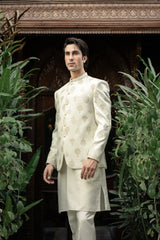 Man wearing a traditional white sherwani with intricate patterns in a decorative setting.