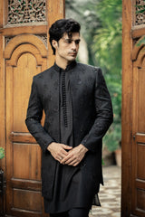 Man wearing a black embroidered sherwani standing in front of wooden doors.