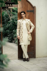 Man wearing a traditional cream sherwani with floral patterns in an outdoor setting.