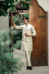 Man in traditional white kurta standing next to a wooden door with greenery in the background