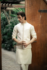Man wearing a traditional cream kurta with intricate patterns, standing against a wooden door.