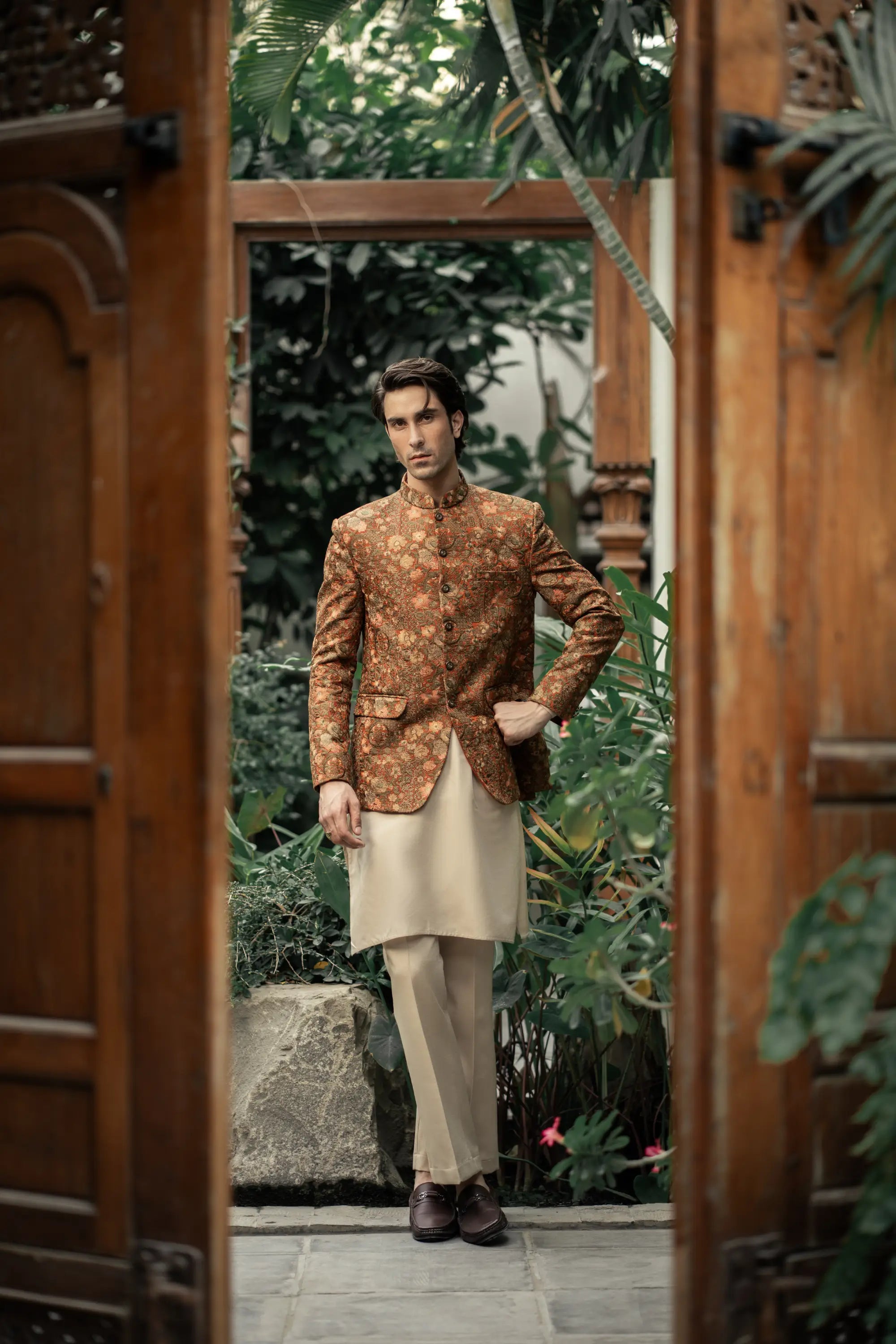 Man in a traditional outfit standing in a doorway with greenery outside