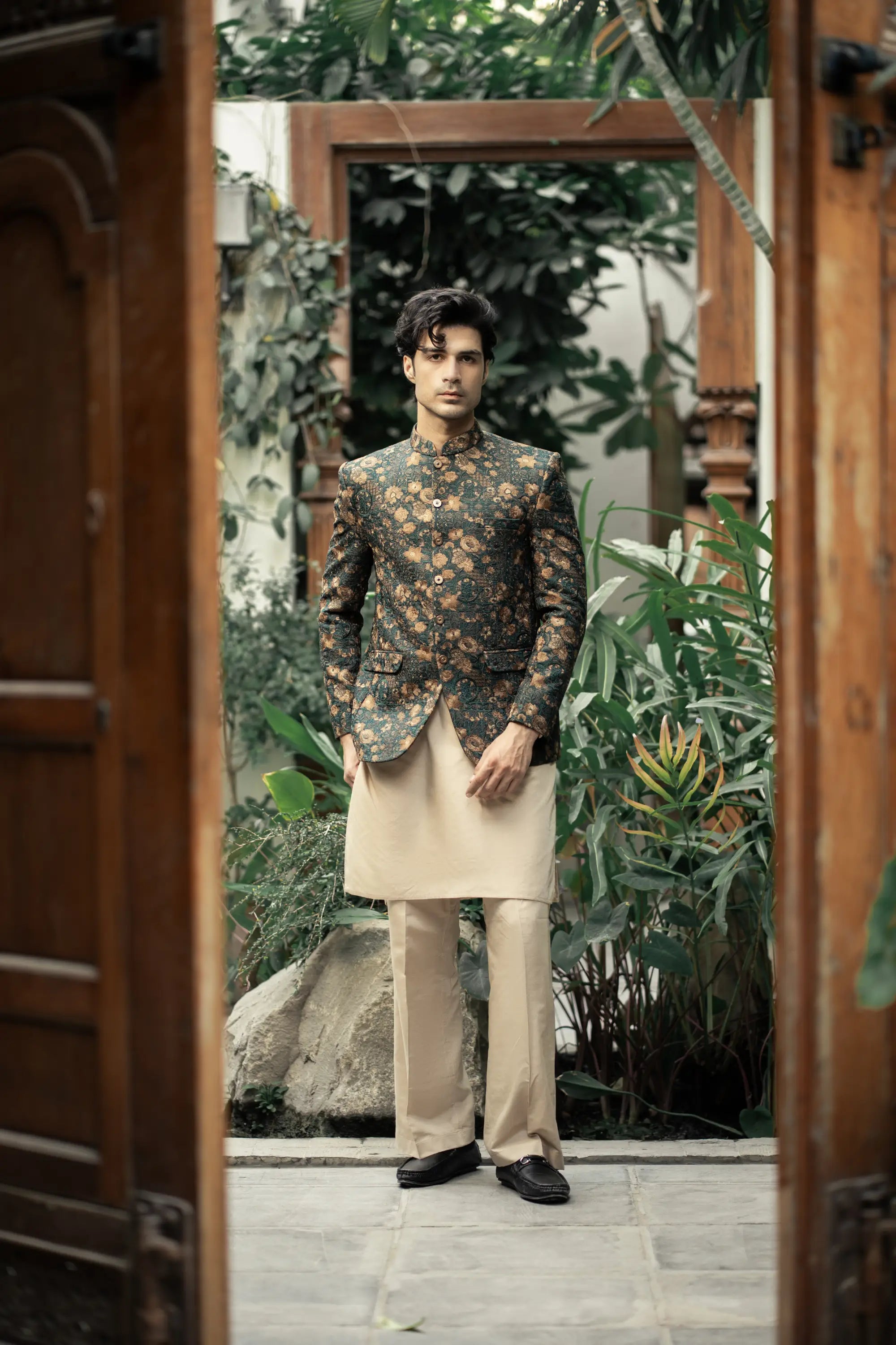 Man in a floral jacket and beige pants standing in a garden setting