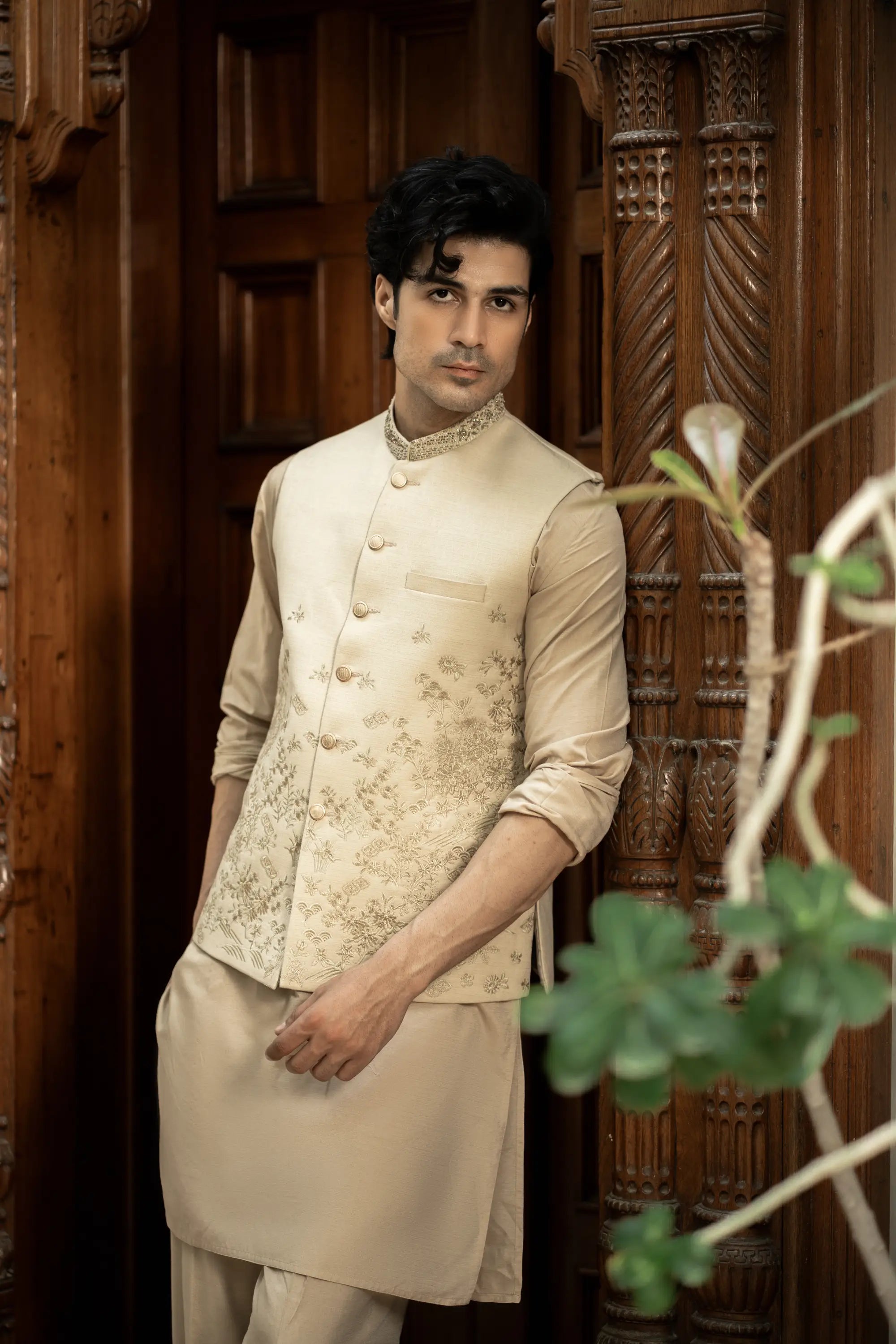 Man wearing a traditional beige kurta with a vest in front of a wooden door.