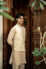 Man wearing a traditional beige kurta with a vest in front of a wooden door.