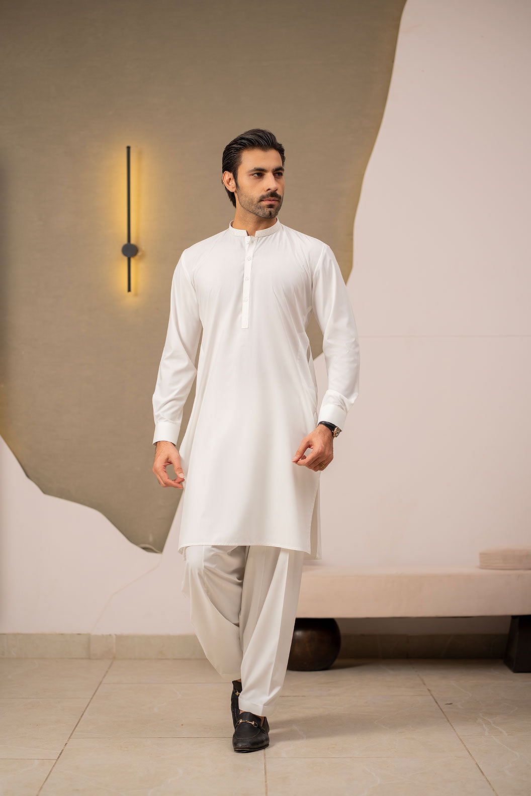 Man wearing a white kurta with beige pants in an indoor setting